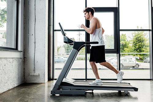 side view of handsome sportsman running on treadmill in gym