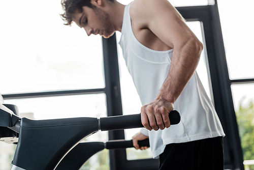 selective focus of tired sportsman touching handrails on treadmill