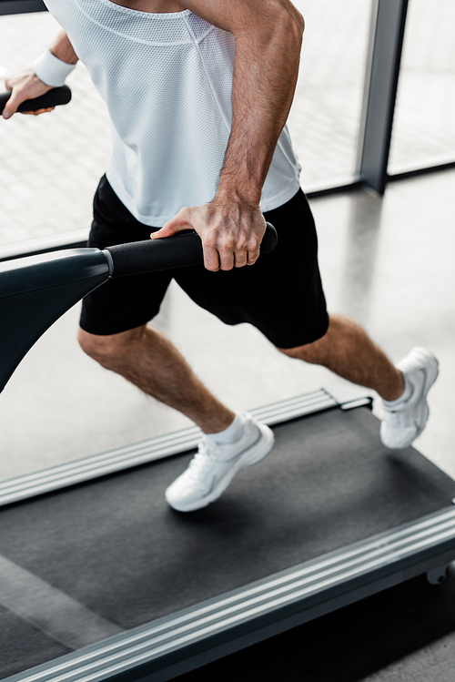 cropped view of tired sportsman touching handrails on treadmill