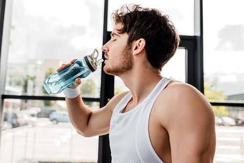 side view of sportsman with closed eyes drinking water and holding sports bottle