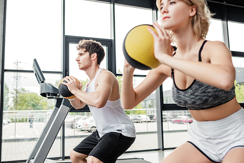 selective focus of handsome and sportive man exercising with ball near girl