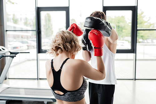 back view of sport couple in boxing gloves and pads exercising in gym