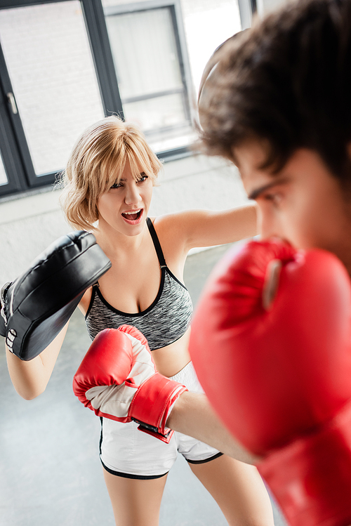 selective focus of emotional girl in boxing pads exercising with sportsman in gym