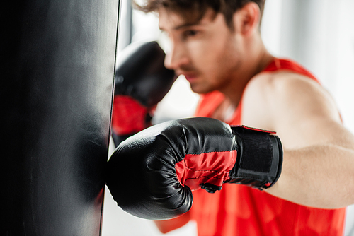 selective focus of athletic boxer in boxing gloves working out with punching bag