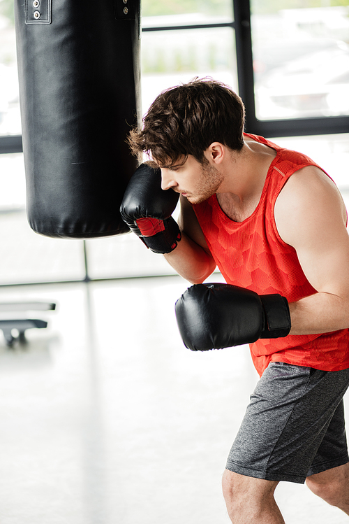 athletic man in sportswear and boxing gloves working out with punching bag