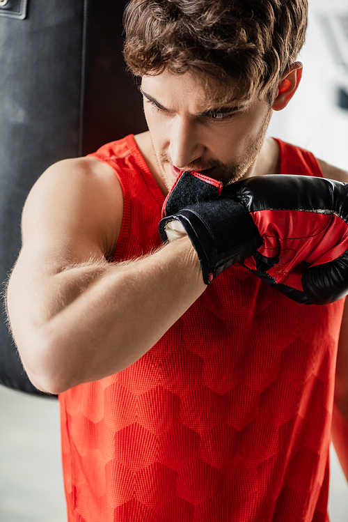 sportsman in sportswear biting boxing glove in gym