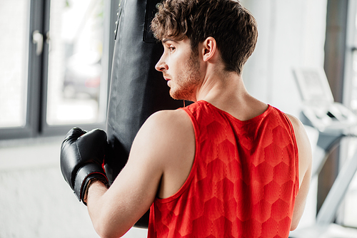 tired man in sportswear and boxing glove touching punching bag in gym