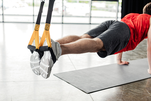 cropped view of athletic man in sportswear exercising with resistance bands on fitness mat