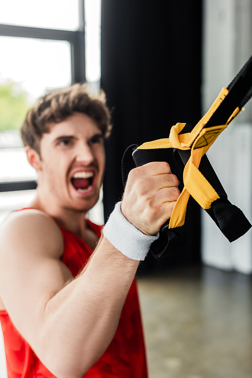 selective focus of sportive man screaming while working out with elastics in gym