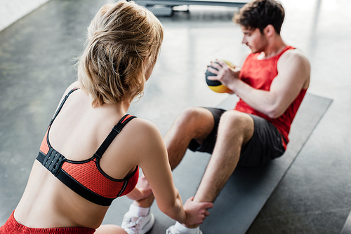 selective focus of sportive girl holding legs of sportsman exercising with ball on fitness mat