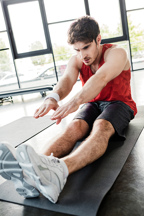 selective focus of handsome sportsman stretching on fitness mat