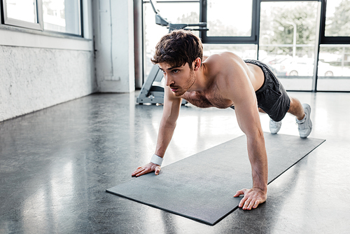 shirtless sportsman doing plank near fitness mat in gym