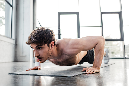 shirtless sportsman doing push ups on fitness mat in gym