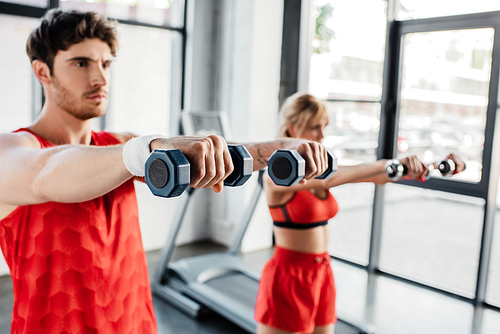 selective focus of sportsman and sportswoman working out with dumbbells in gym
