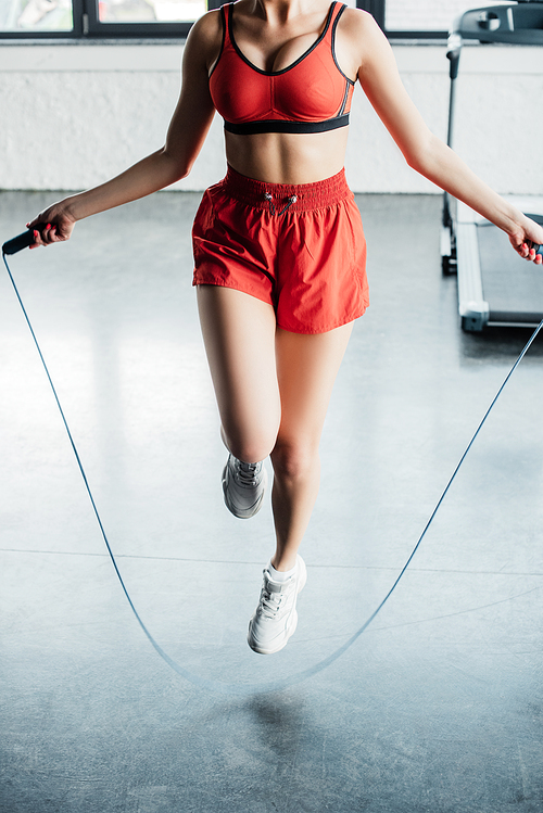 cropped view of sportive girl jumping while holding skipping rope in gym