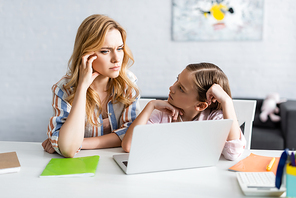 Selective focus of kid looking at thoughtful mother near laptop at home