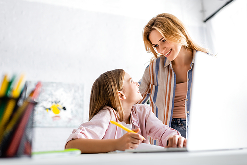 Selective focus of smiling kid looking at mother during online education at home