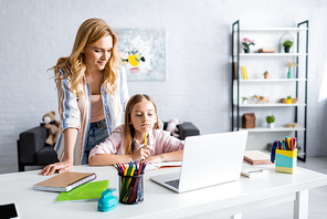Selective focus of mother standing near thoughtful daughter during online education