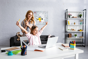 Smiling woman standing near happy child showing yeah gesture during online education
