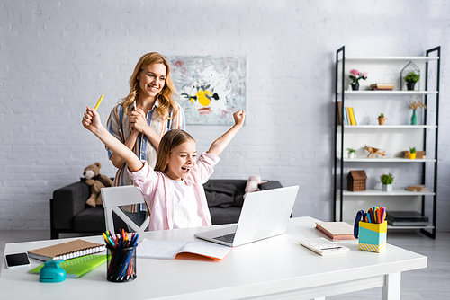 Smiling woman standing near happy child showing yeah gesture during online education