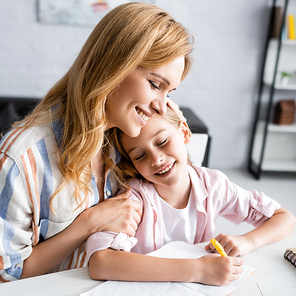 Smiling mother embracing kid writing on notebook at table