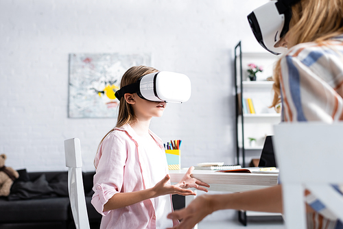 Selective focus of kid using vr headset near mother and stationery on table