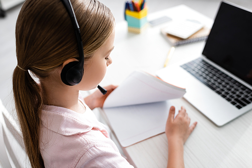 Selective focus of child in headset holding copy book during electronic learning