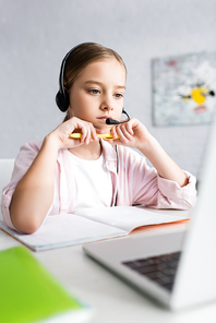 Selective focus of child in headset holding pen and looking at laptop