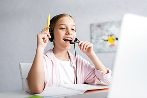 Selective focus of positive kid in headset having idea during online education at home