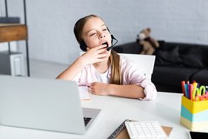 Selective focus of sleepy kid in headset yawning during electronic learning at home