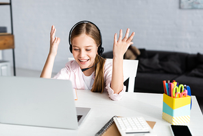Selective focus of positive child in headset looking at laptop near stationary on table