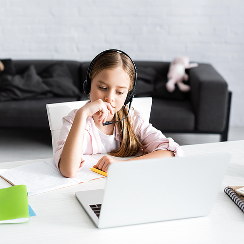 Selective focus of cute kid in headset sitting near notebook and laptop on table