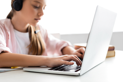 Selective focus of kid in headset typing on laptop at home