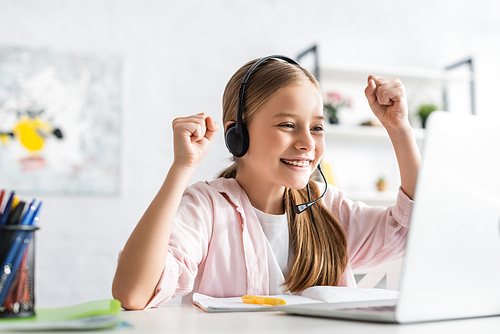 Selective focus of smiling child in headset showing yes gesture during online education at home
