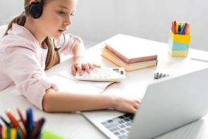 Selective focus of kid in headset using laptop and calculator during online education