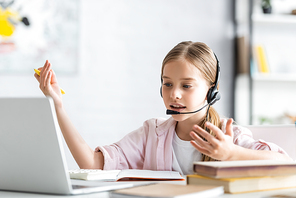 Selective focus of child in headset talking during webinar near books at home