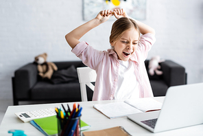 Selective focus of kid yawing and stretching beside laptop and stationery on table
