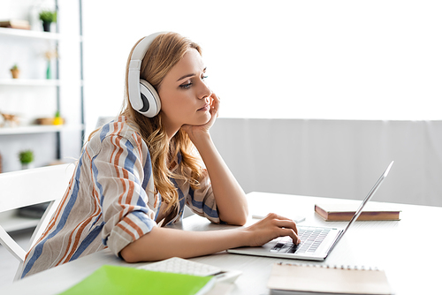 Selective focus of pensive woman working with laptop and headphones