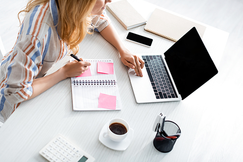 Overhead view of adult freelancer working with laptop and notebook