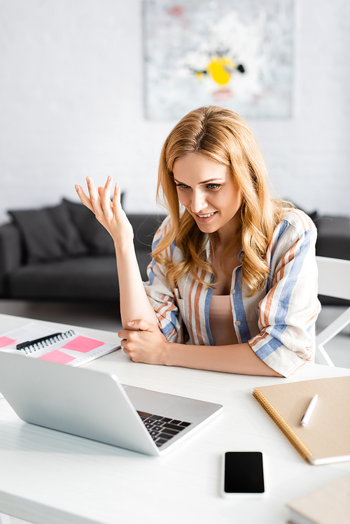 Selective focus of woman talking during webinar near notebooks at home