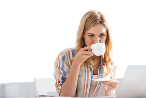Selective focus of pretty woman drinking coffee while working with laptop