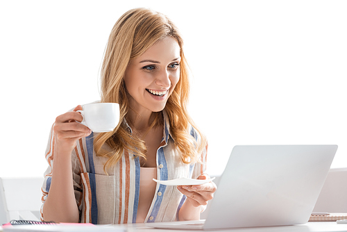 Selective focus of woman smiling to laptop and holding cup
