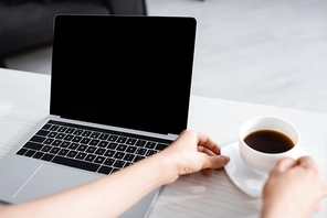 Cropped view of woman hands holding cup of coffee and laptop