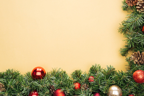 top view of christmas tree branch with red and golden baubles on yellow background