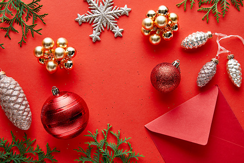 top view of shiny Christmas decoration, envelope and thuja on red background