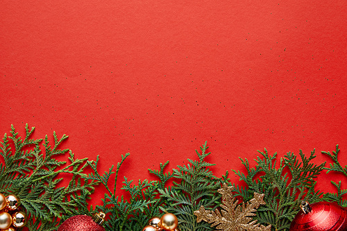 border of shiny Christmas decoration on green thuja branches on red background with copy space