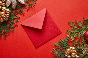 top view of red envelope near shiny Christmas decoration on green thuja branches on red background