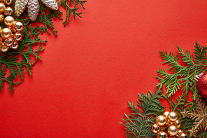 top view of shiny Christmas decoration on green thuja branches on red background with copy space