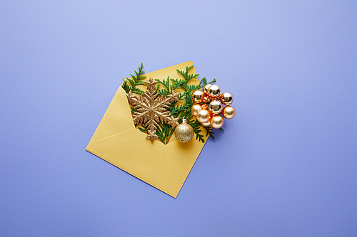 top view of envelope with shiny golden Christmas decoration and green thuja branches on blue background