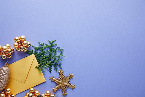 top view of shiny golden Christmas decoration, green thuja branches and envelope on blue background with copy space
